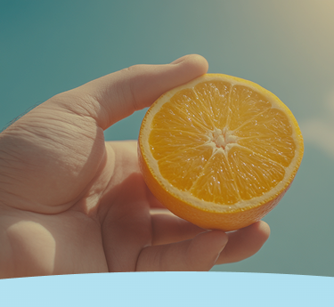 Mão segurando uma laranja cortada ao meio em um fundo de céu azul.