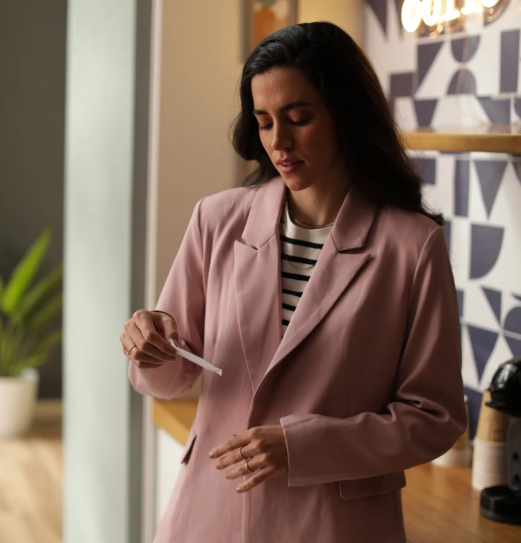 Uma mulher com um blazer rosa olha para uma tira de teste em uma sala moderna.