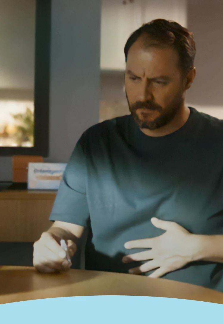 Homem com a mão na barriga segurando Enterogermina 2-4 bilhões / 5 ml de suspensão oral.