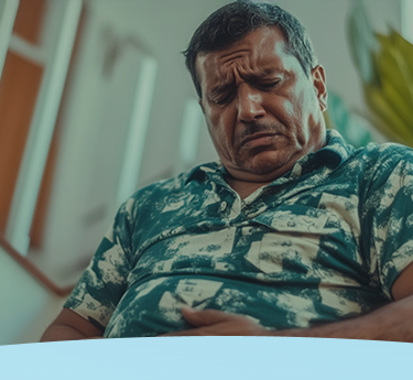 Homem sentado com uma expressão de dor, segurando o estômago.