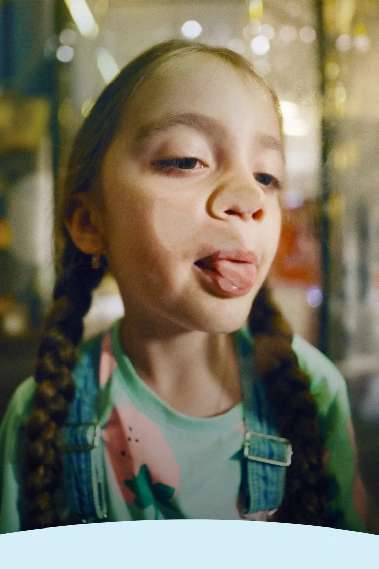 Criança com tranças enfiando a língua para fora através de uma janela de vidro.