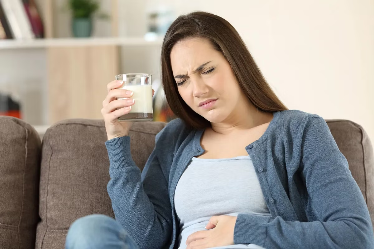 Mujer que sufre de intolerancia a la lactosa, sosteniendo un vaso de leche y mostrando malestar estomacal.