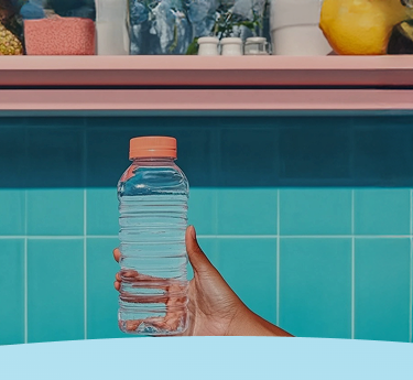 Mão segurando uma garrafa transparente em frente a uma parede de azulejos turquesa com uma prateleira acima.
