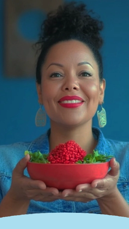 Mulher segurando uma tigela vermelha cheia de frutas vermelhas e verduras, sorrindo para a câmera.