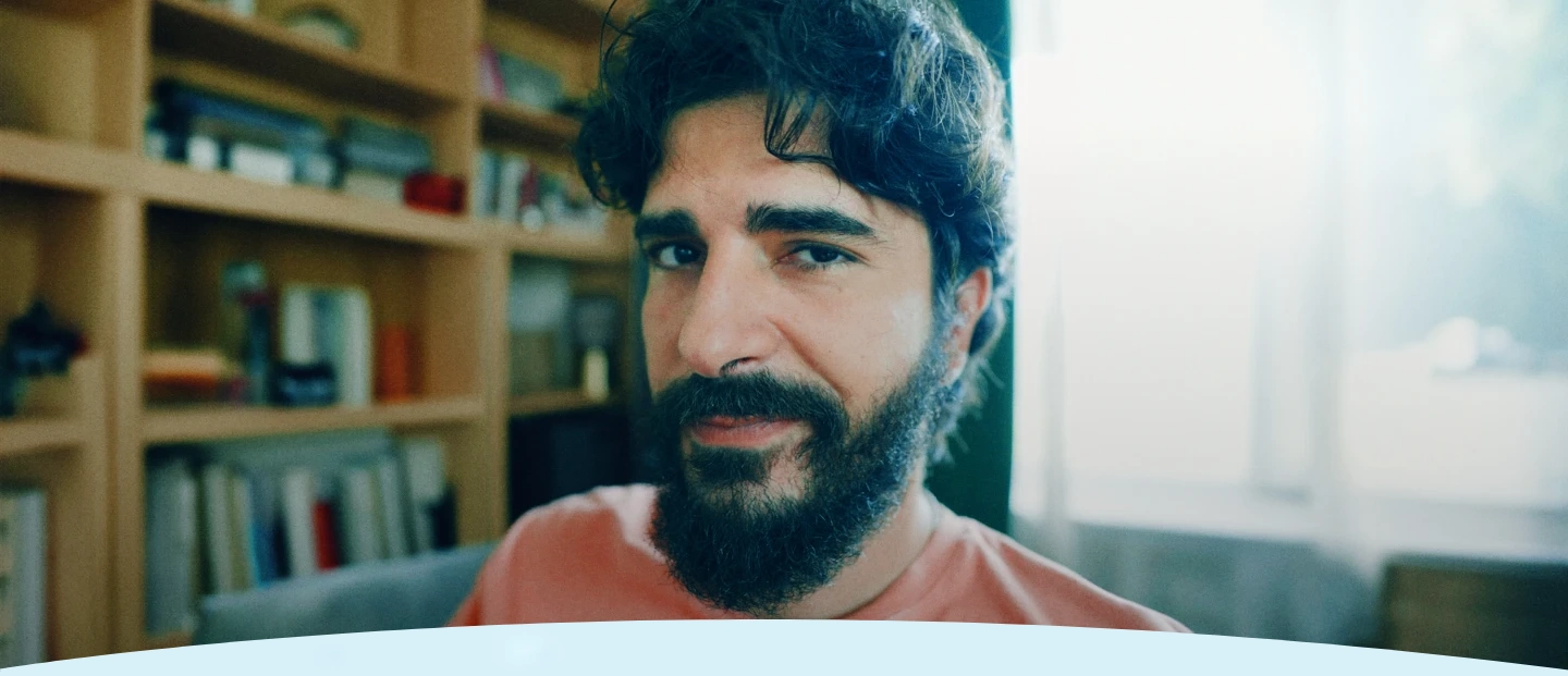 Homem com barba e cabelos cacheados em frente a uma estante de livros.