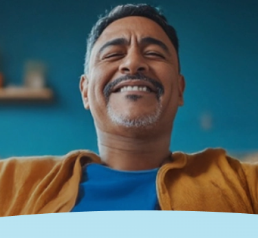 Homem sorridente em uma roupa azul e marrom contra um fundo azul.