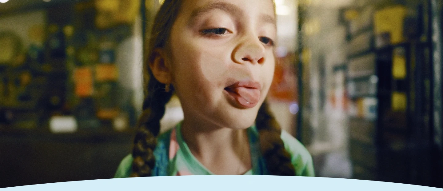 Criança com tranças enfiando a língua para fora através de uma janela de vidro.