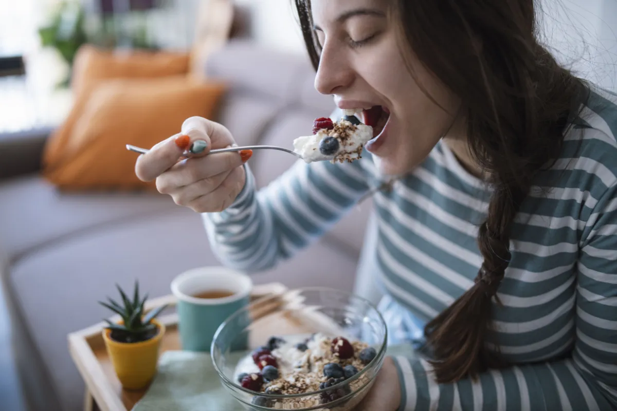 Mujer feliz desayunando un yougurt con frutos rico en probióticos.