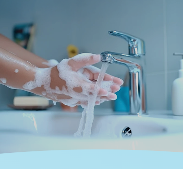 Mãos ensaboadas com sabão sob água corrente na pia do banheiro.