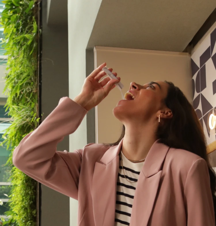 Uma pessoa com um blazer rosa tomando um líquido de um pequeno frasco.