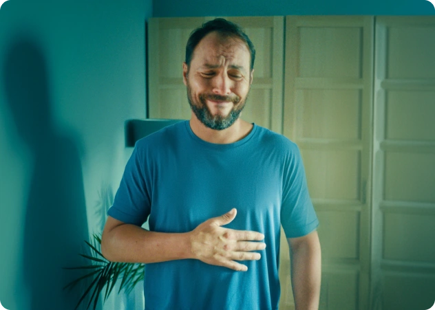 Homem de camisa azul segurando o estômago com uma expressão de dor.